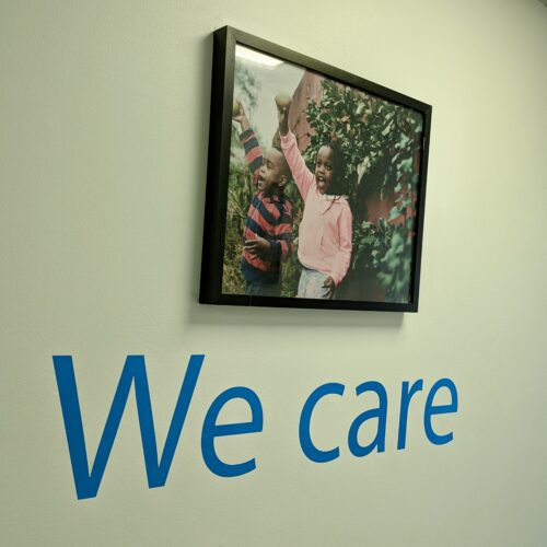 A framed photo of two smiling young children is hanging on a wall. Underneath there is a wall decal that says 'We care'.
