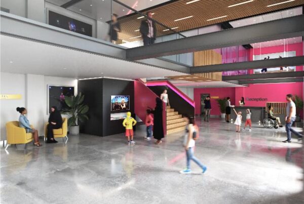A rendered image of the new foyer of the Bradford Arts Centre, with a shiny grey floor, a seating area, mezzanine level with glass barrier above, and magenta pink paint across half of the visible walls.