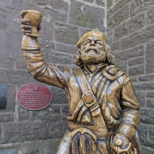 Photograph of a wooden carved statue of Rob Roy raising a toast, situated outside Crieff and Strathearn Museum.